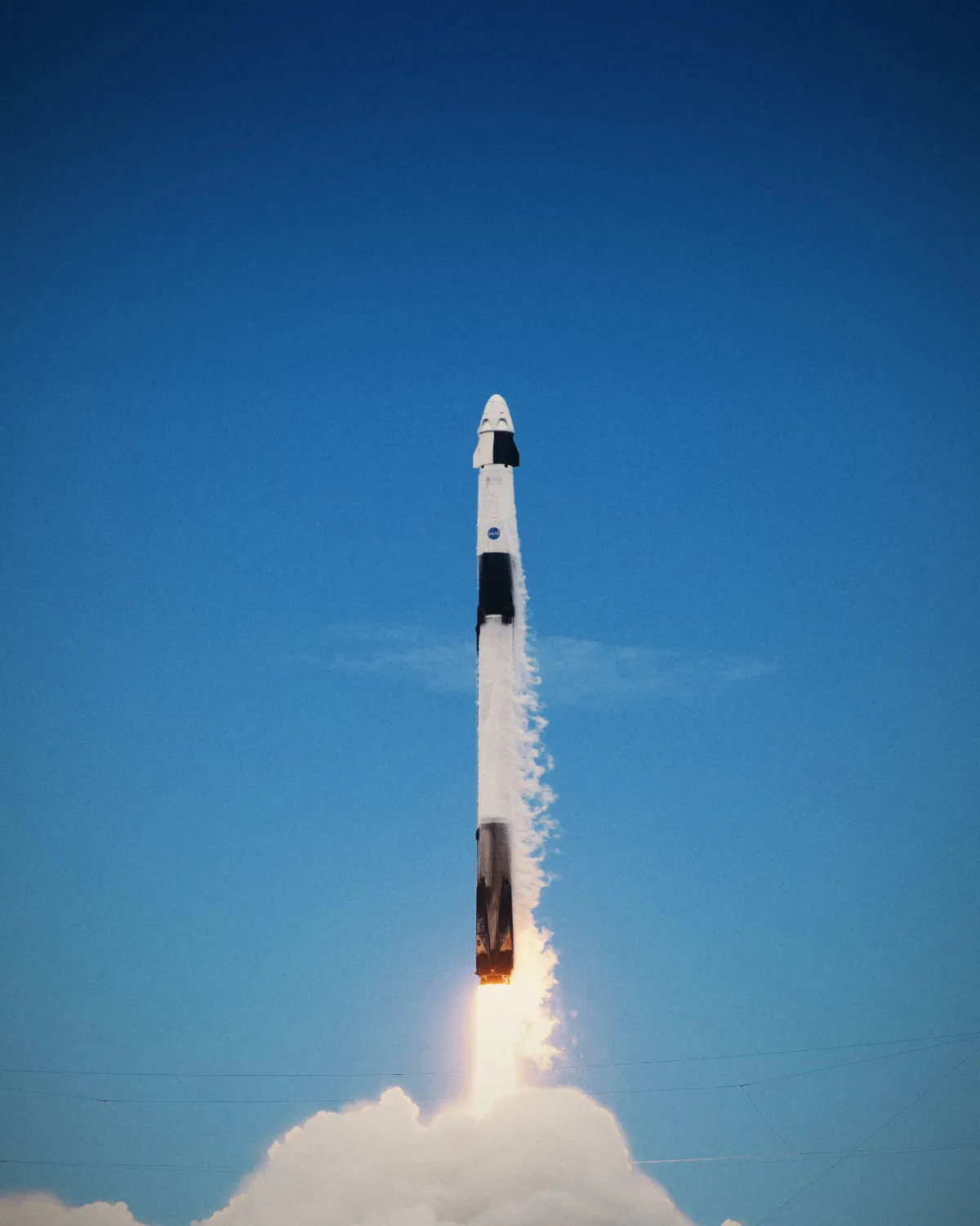 A Falcon 9 rocket with a Dragon capsule lifts off into a clear blue sky