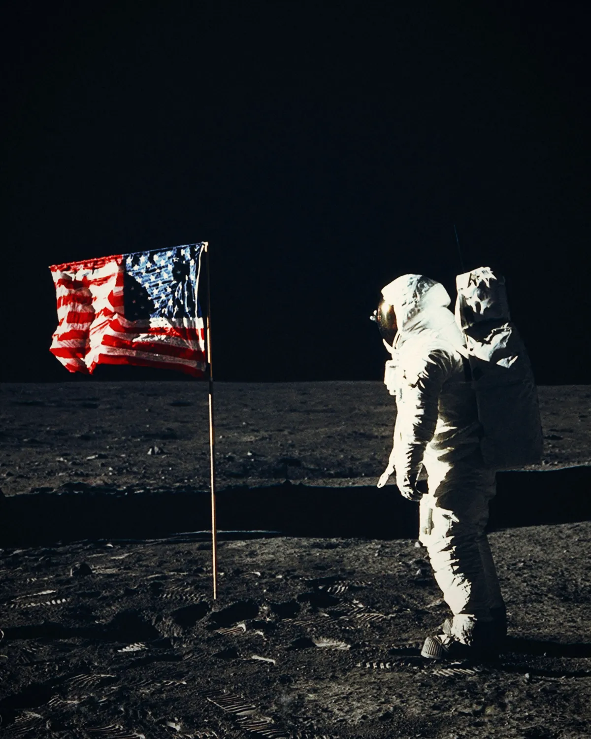 An astronaut stands beside the American flag on the surface of the Moon